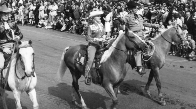 A black and white photograph of Patsy Rodgers riding a horse alongside two other Stampede officials in 1946.