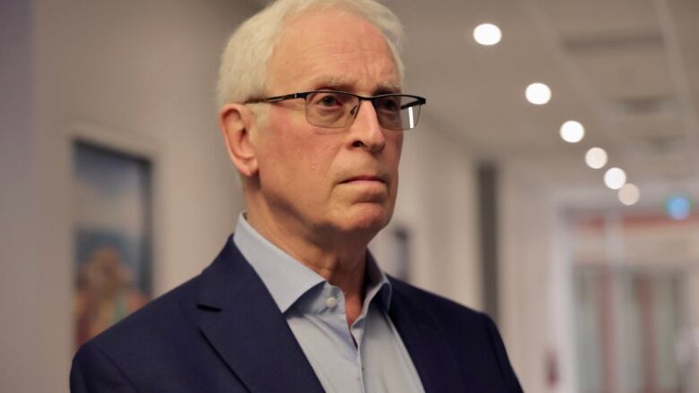 A man with white hair wearing a blue shirt and a blazer is seen in semi-profile