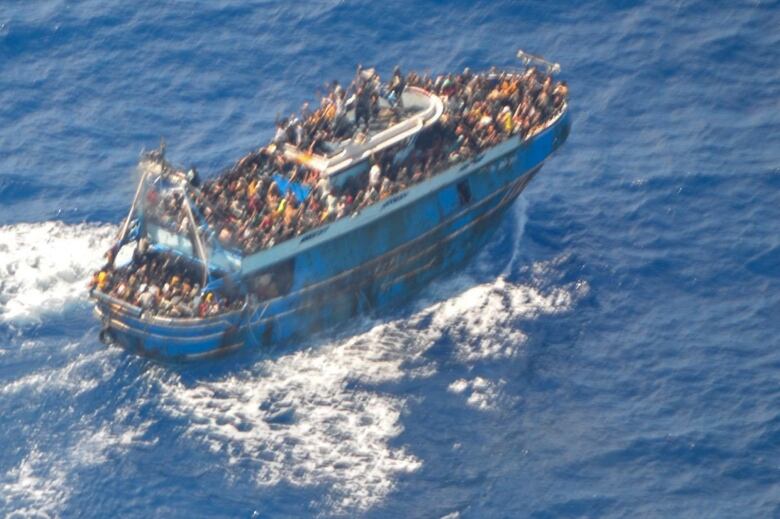 A blurry image shows dozens of people on the deck of a battered blue fishing boat in the Mediterranean Sea. 