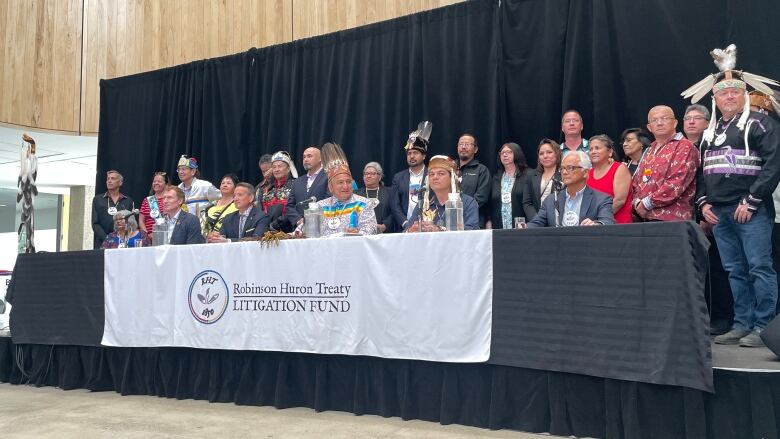 People sitting at a table, some are wearing traditional indigenous regalia.