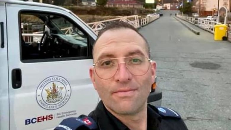 A paramedic stands in front of an ambulance with a rainbow in the distance behind him.