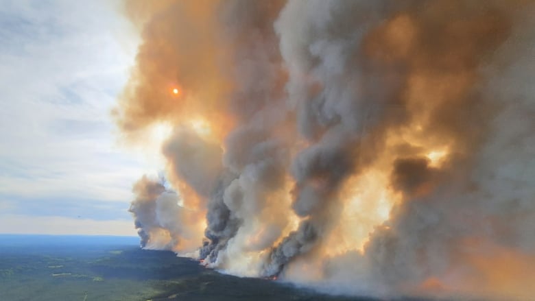 Plumes of orange and grey smoke rise from a large wildfire.