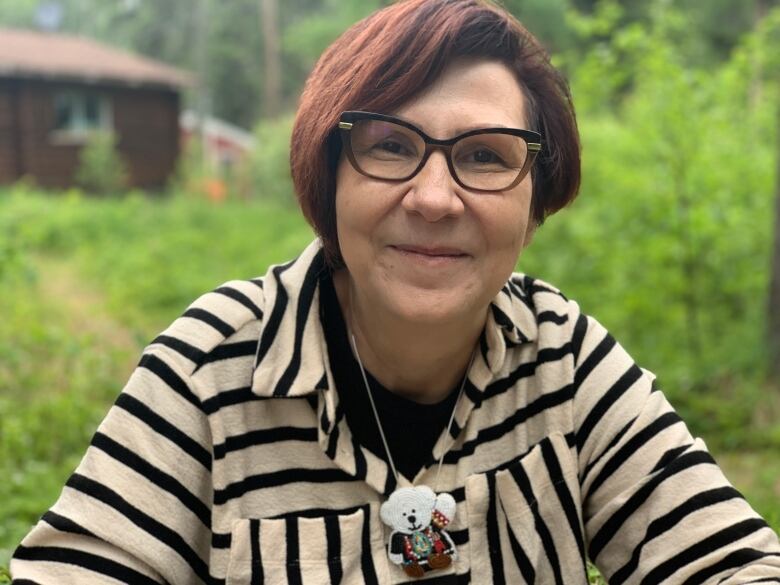 A woman in glasses and a black and white striped top wearing a beaded white bear medallion smiles for the camera.