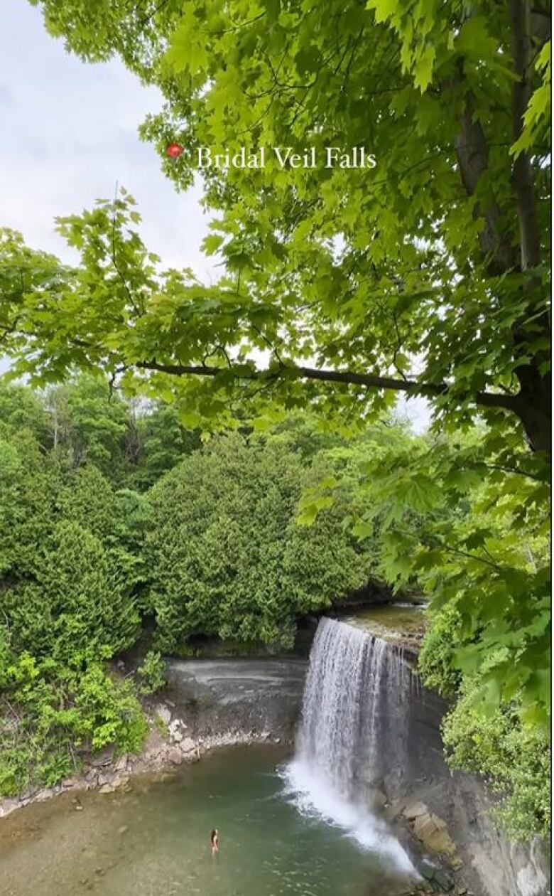 A woman standing the water in front of a popular waterfall on Manitoulin Island in Ontario.