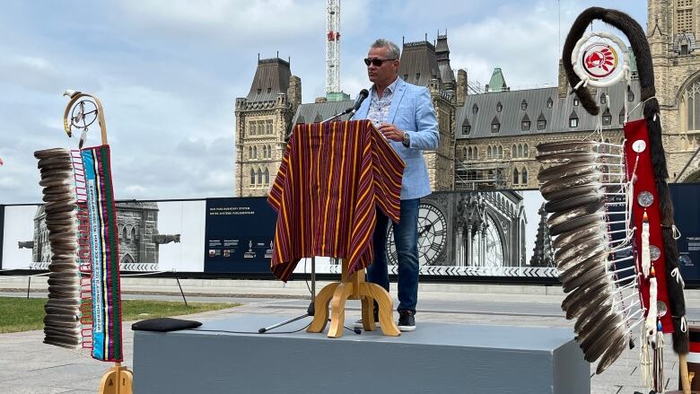 A man speaks at a podium with Parliament Hill's Centre Block in the background.