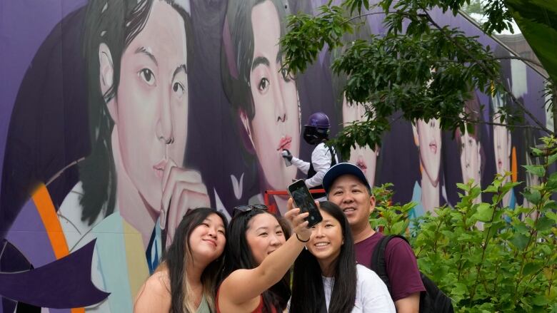 Four young people take a selfie in front of an outdoor mural.