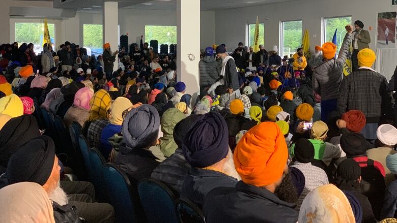 Hundreds of people are seen in a packed temple room, many of them wearing turbans.