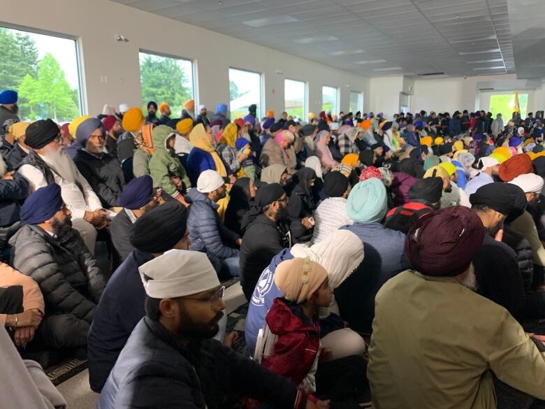 Dozens of people, many of them wearing turbans, are seen in a large room.