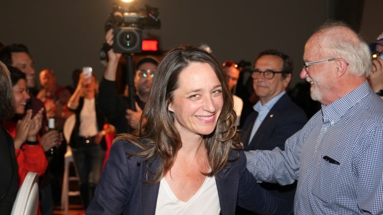 Smiling woman surrounded by people and cameras.