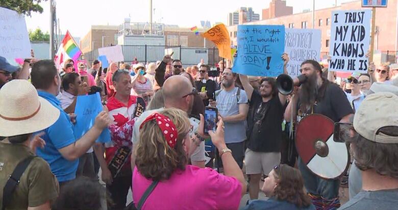 Dozens of people are on a street holding posters and pride flags. 