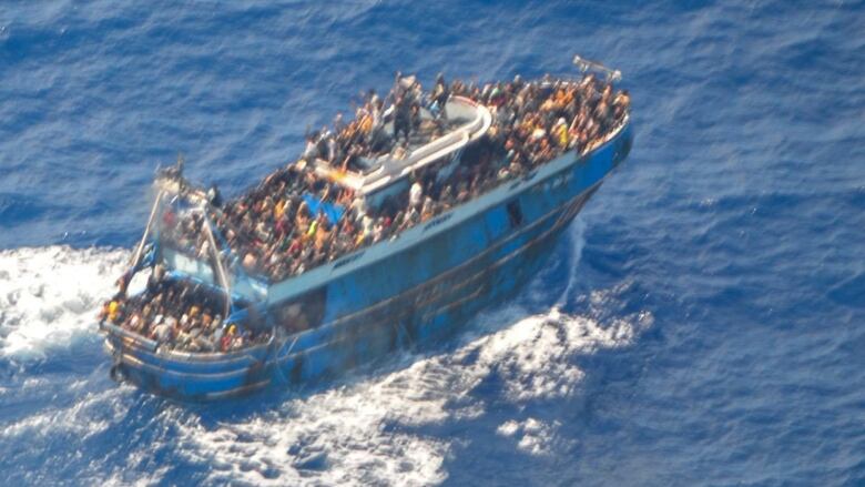 An aerial shot of a boat in the sea filled with people is shown.