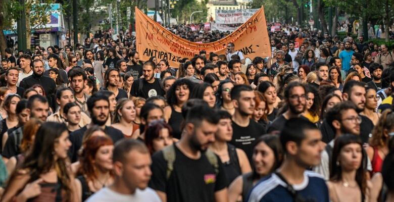 A street full of people, some holding signs, is shown.