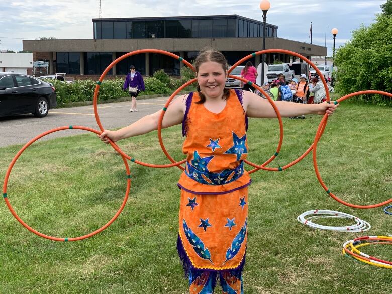 A girl in orange regalia holds up five orange hoops.