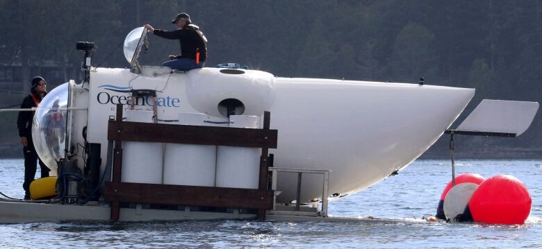 A man in a baseball hat emerges from the open hatch of a white submersible with the words OceanGate written on the side. 