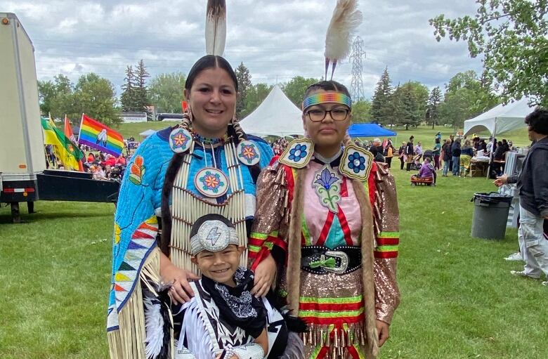 Two women and a young child pose for a photo while wearing their powwow regalia.