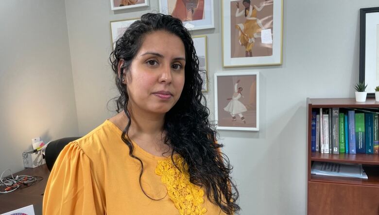 A woman in a yellow top looks at the camera. An office decorated with books and artwork is in the background. 