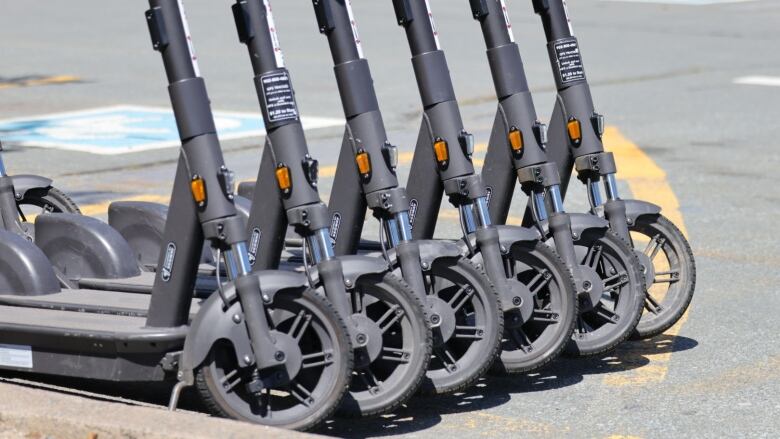 A line of multiple grey scooters are seen from the handlebars down in a lot