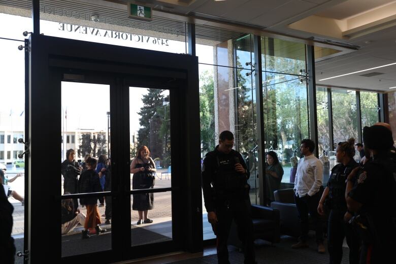 Organizers are seen outside the doors of Regina city hall as police officers and Coun. Dan LeBlanc (white shirt) look on from inside the building. 