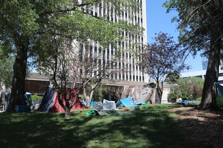 Tents, hammocks and sleeping bags are positioned in front of a multi-storey cement building. 