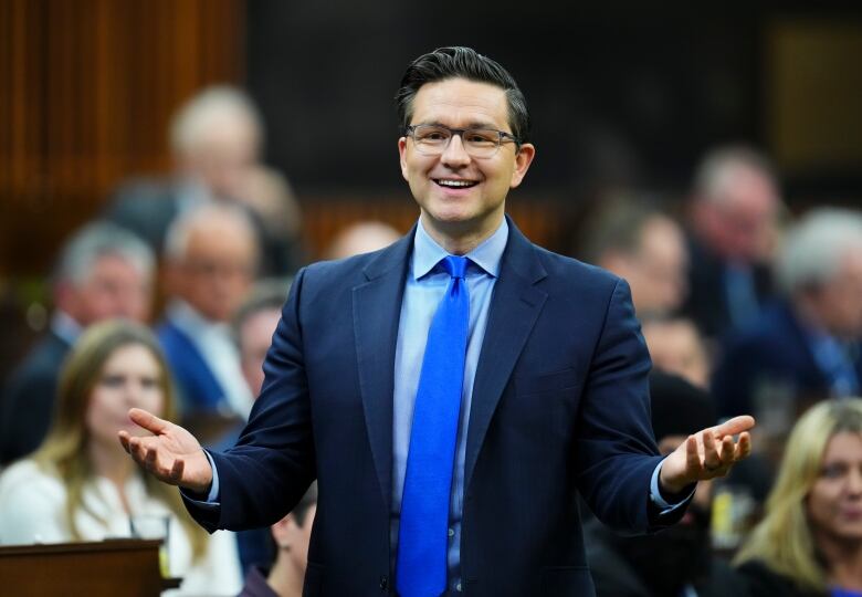 A man in a suit smiles and gestures.