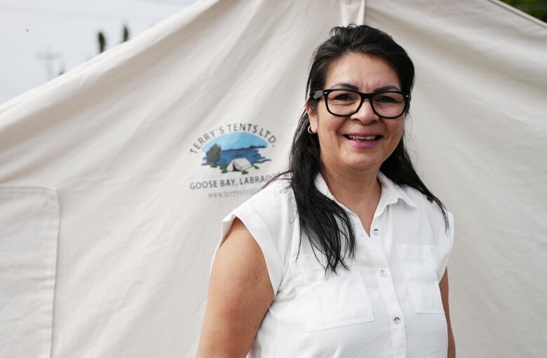 A woman in a white shirt stands in front of a tent. 