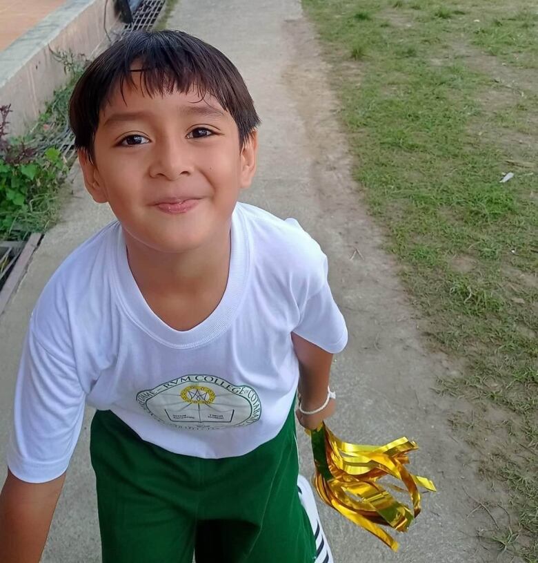 A boy is playing outdoors and looking straight at the camera with a smile on his face.