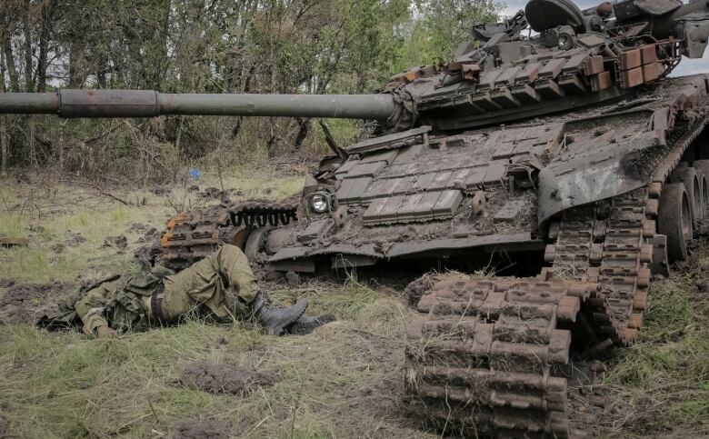 The body of a soldier is shown near a destroyed tank.