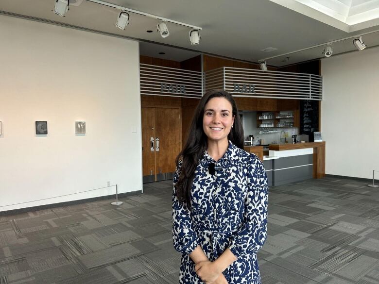 A woman stands inside an office space and smiles. 