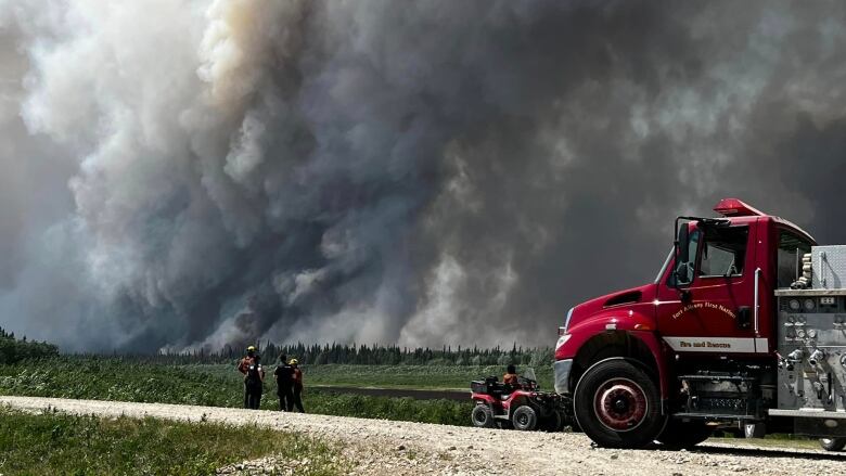 A fire truck is parked on a gravel road with a wall of smoke in the background