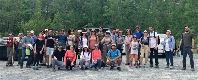 A large group poses together in front of a stand of trees.