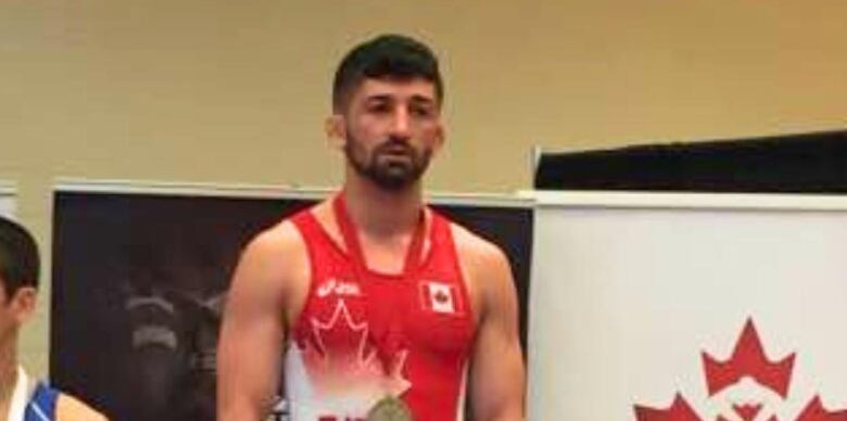 A man with short black hair stands in a red leotard on a podium.