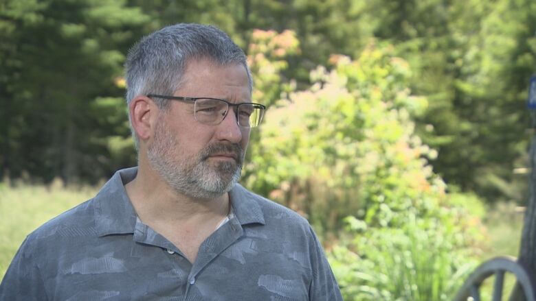 A man with facial hair in a grey shirt is seen in profile.