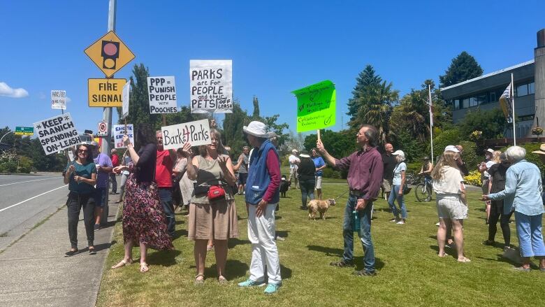 A group of protestors and dogs on a lawn carrying signs.