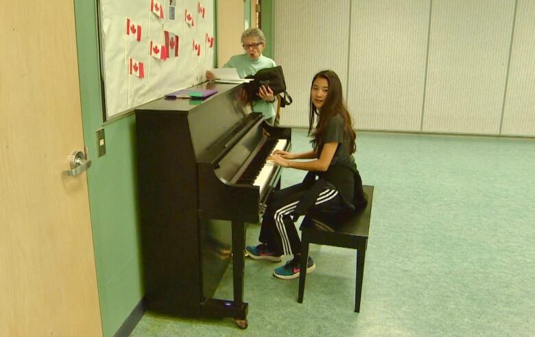 A Grade 6 students plays piano for a senior who is singing.