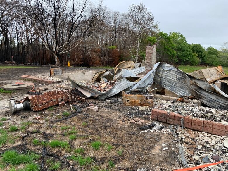 Kasey DeMings' home ruined by fire. All that remains is a foundation, two toppled chimneys, and the twisted remains of the metal roof. 