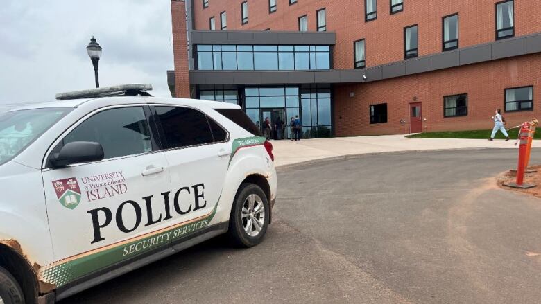 Security car stands outside a tall building with about a dozen people seen entering the building's doors behind it. 