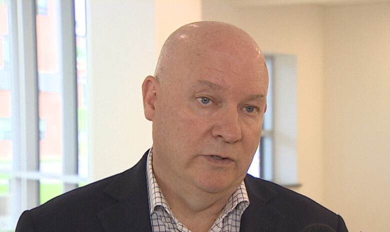 Bald man in open shirt and business jacket speaks into a CBC microphone. 