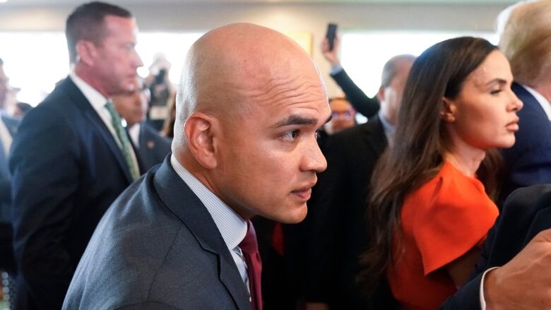 A closeup of a bald man in a suit is shown.