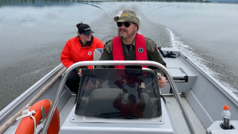 A man driving a small boat on a river with a woman sitting behind him