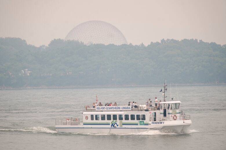 A boat travels down a body of water with smoky skies in the background.