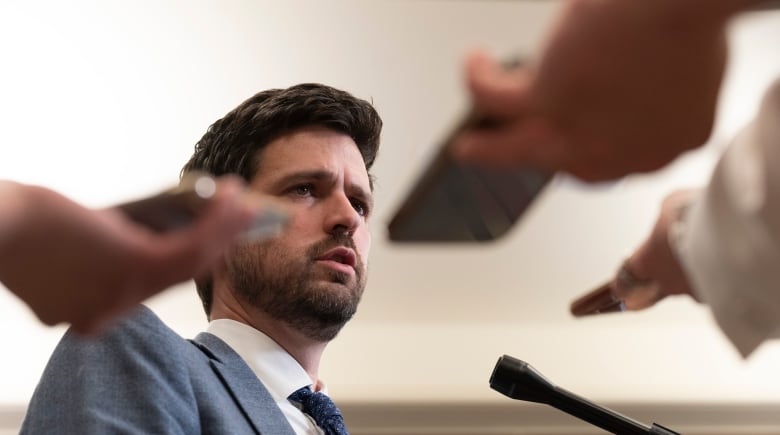 Reporters hold up recording devices as Immigration Minister Sean Fraser speaks.