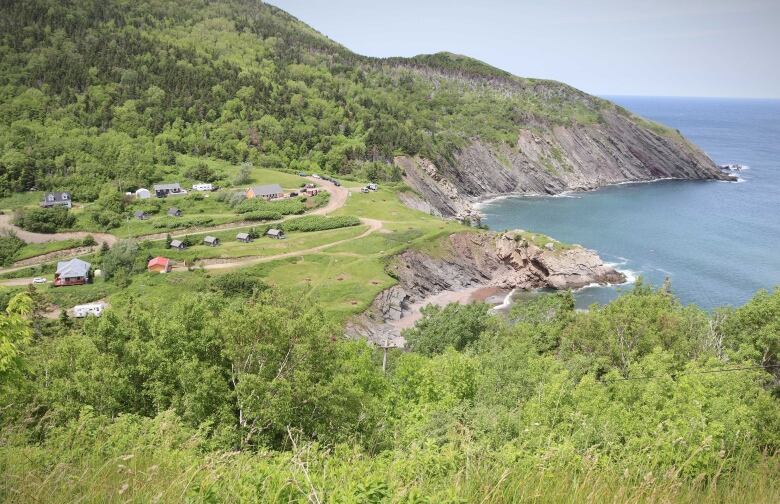 View looks down a lush green mountain onto a campground situated on a cliff overlooking the ocean.