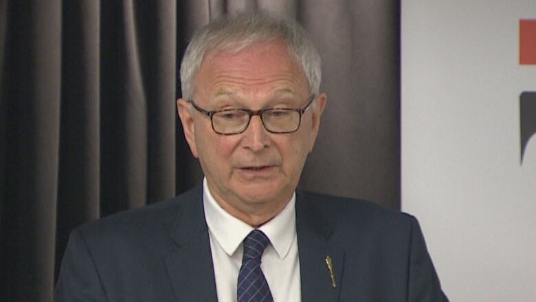 A man with grey hair and glasses wearing a suit and standing at a wooden podium.