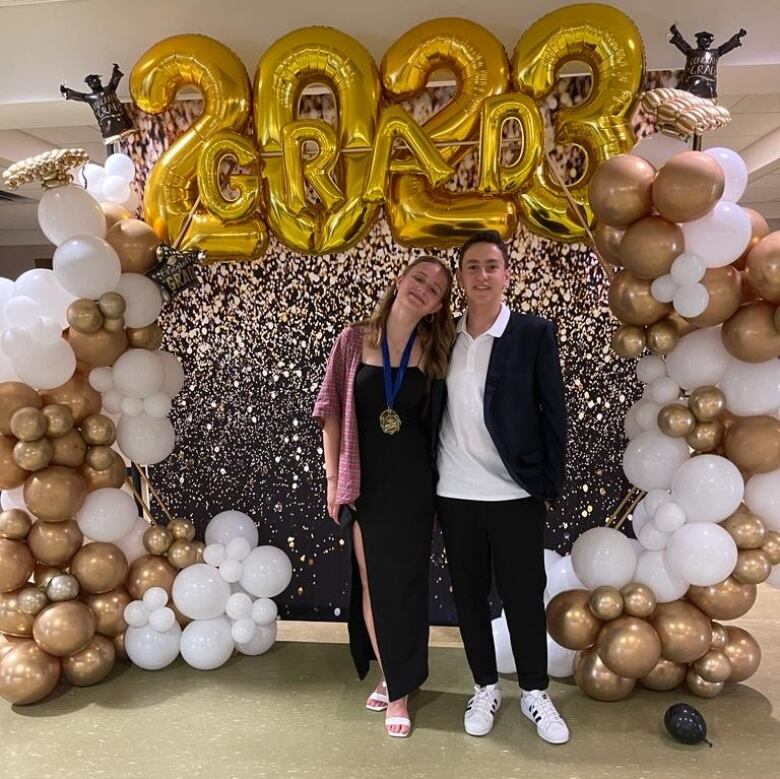 Two teens stand in front of balloons at a graduation ceremony 