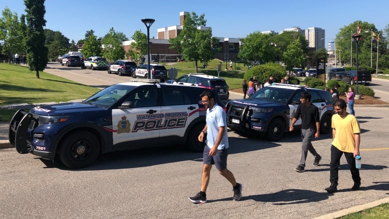 People walk past police cars at the University of Waterloo.