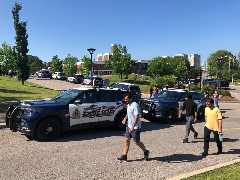 People walk past police cars at the University of Waterloo.