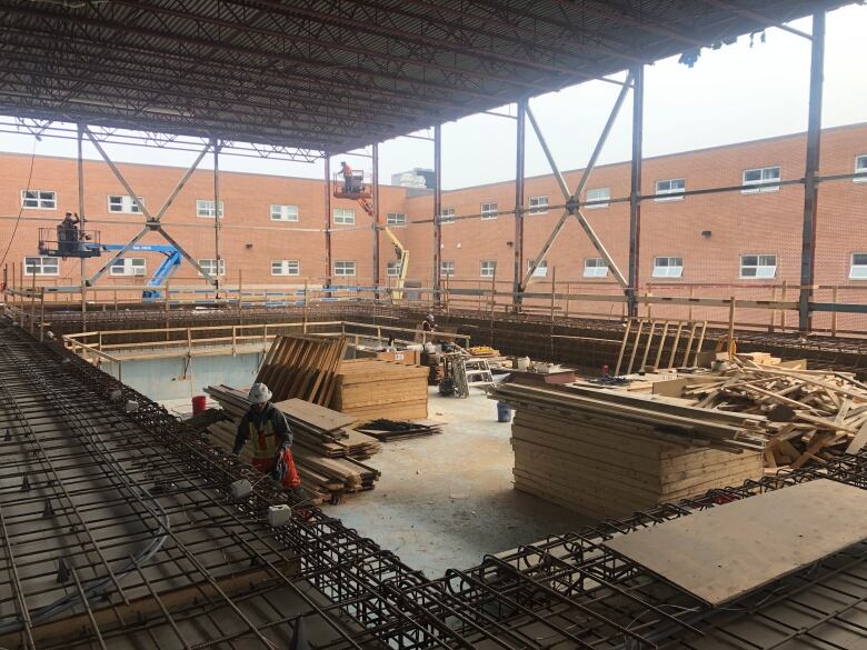 A large empty pool construction site with steal beams surrounding the open walls. Large piles of materials and tools sit in the middle. 