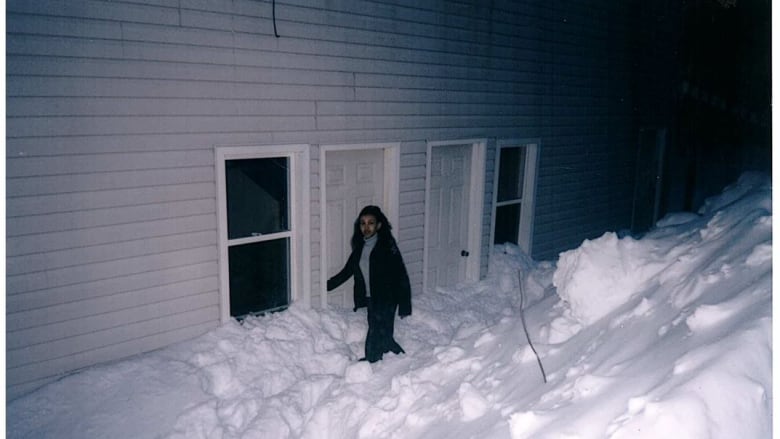 A woman walks through piles of snow to get to an apartment door.