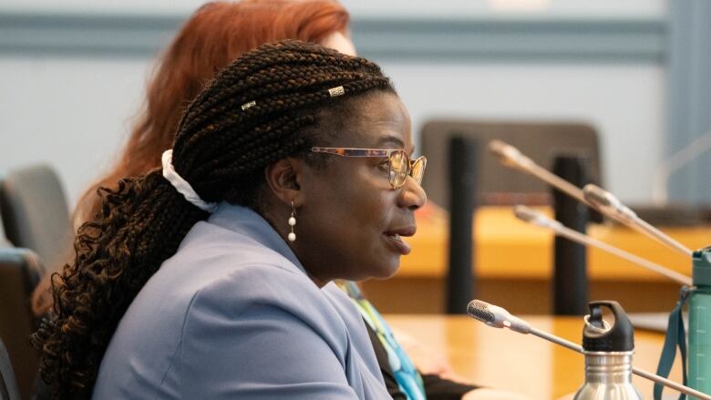 A woman sits at a table and speaks into a microphone.