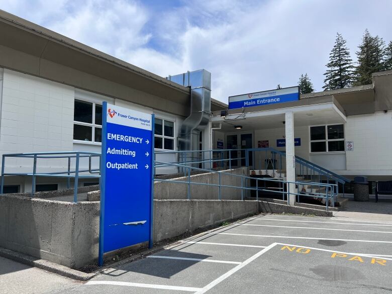 A small L-shaped bungalow with a blue Fraser Health standalone sign that says EMERGENCY, Admitting and Outpatient leads to an entrance above which reads: Main Entrance.